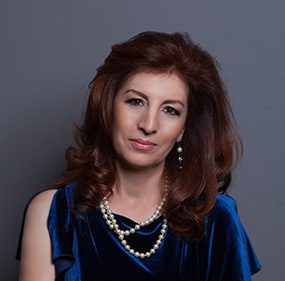 Woman in blue dress with pearl necklace.